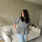Woman standing in a living room wearing a checkered top and jeans.