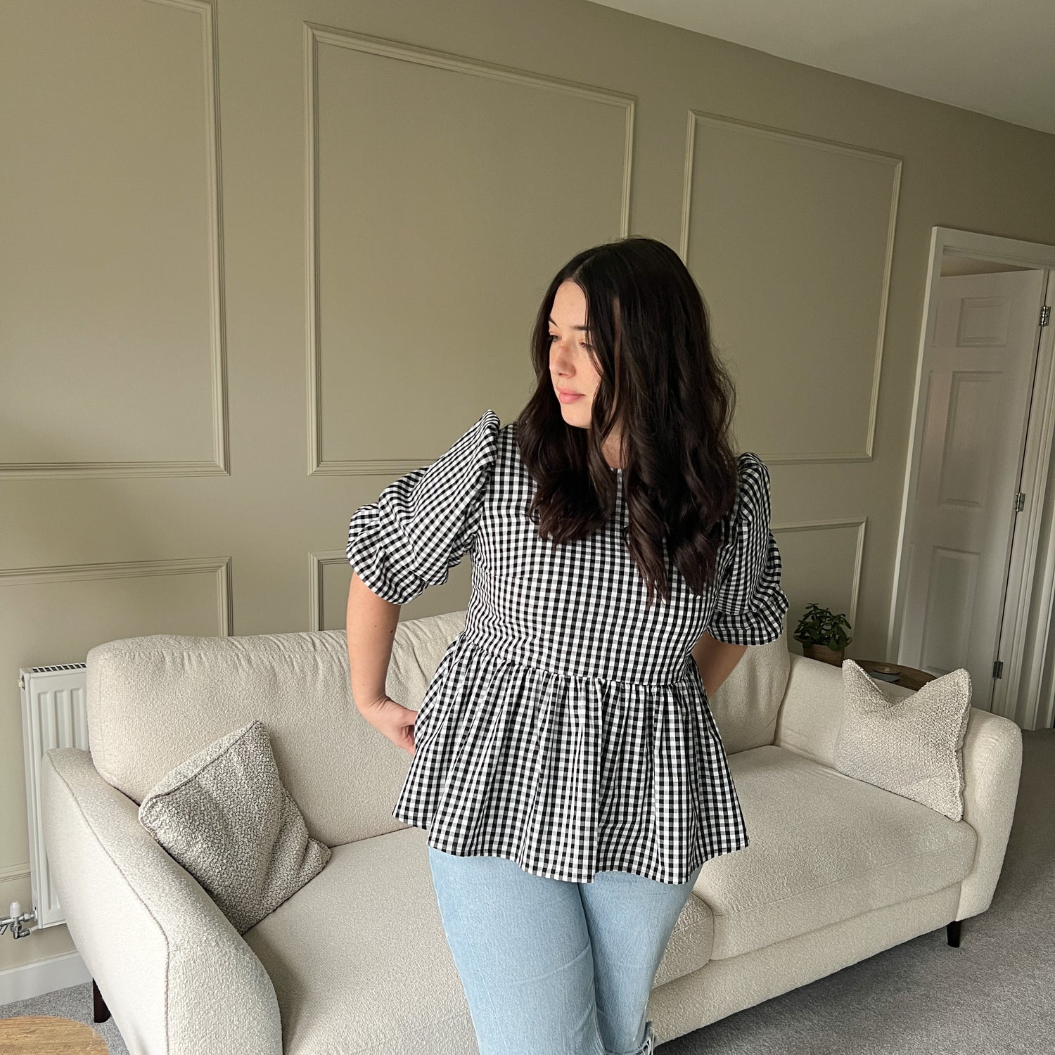 Woman standing in a living room wearing a checkered top and jeans.